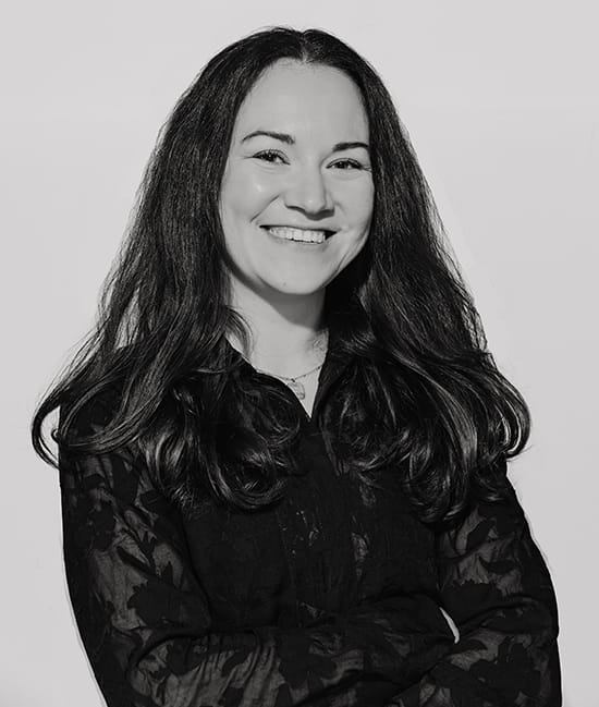 Marketing 14 Junge Frau mit langen Haaren und schwarzem Hemd lächelt vor weißem Hintergrund.