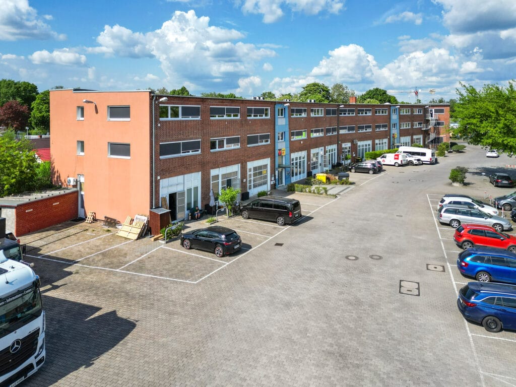 Leasing - Feevr 3 Gewerbegebäude mit Parkplatz bei sonnigem Wetter und blauem Himmel im Hintergrund.